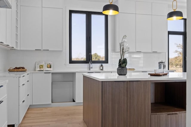 kitchen with light wood-type flooring, light countertops, hanging light fixtures, white cabinets, and modern cabinets