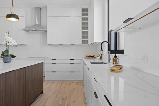 kitchen with light stone counters, a sink, white cabinetry, wall chimney exhaust hood, and modern cabinets