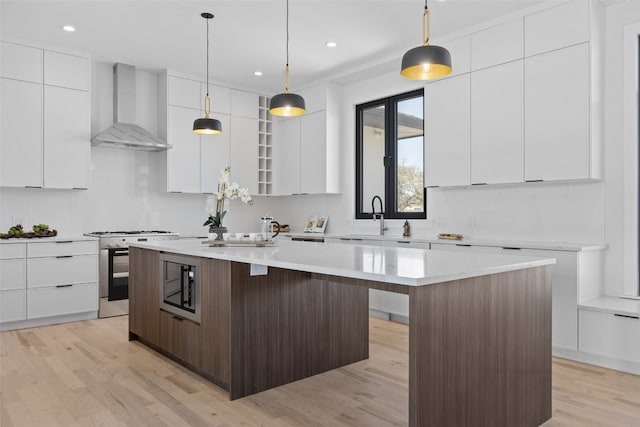 kitchen with modern cabinets, a kitchen island, stainless steel appliances, white cabinets, and wall chimney range hood