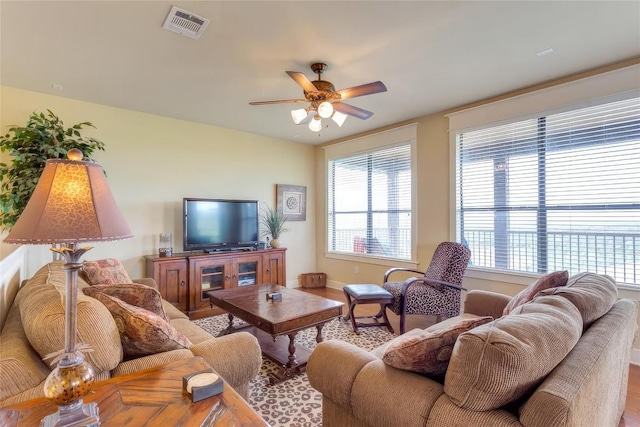 living room featuring wood finished floors, visible vents, baseboards, and ceiling fan