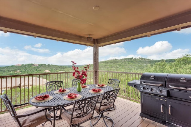 wooden terrace with outdoor dining area, a view of trees, and grilling area