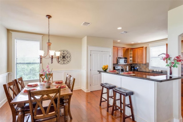 dining room featuring a chandelier, visible vents, light wood-type flooring, and a wainscoted wall