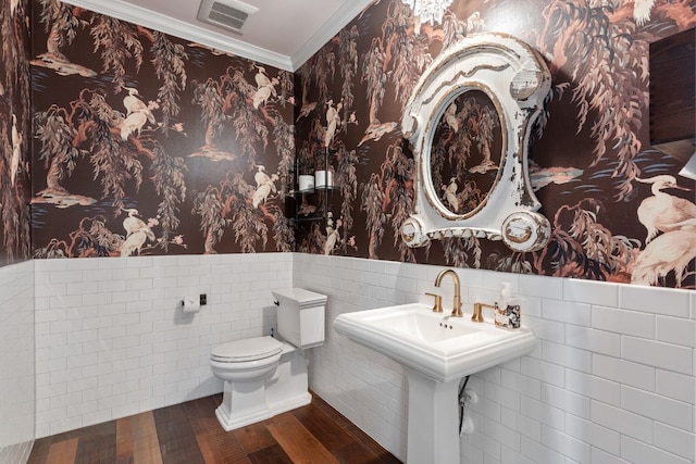 half bath with visible vents, wallpapered walls, wainscoting, crown molding, and toilet