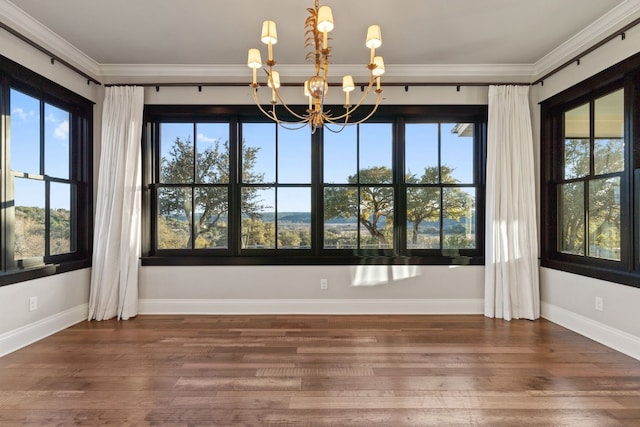 unfurnished dining area featuring a notable chandelier, ornamental molding, baseboards, and wood finished floors