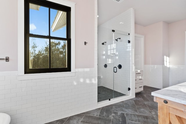 full bath with a wainscoted wall, a shower stall, tile walls, and vanity