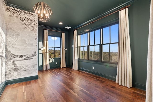 spare room with a notable chandelier, wood-type flooring, baseboards, and ornamental molding