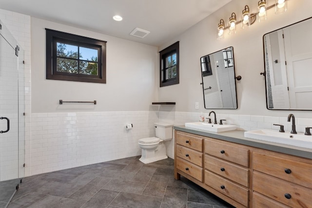 bathroom with double vanity, wainscoting, a stall shower, tile walls, and a sink