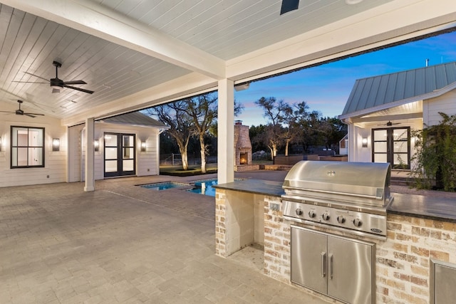 patio terrace at dusk with a storage structure, exterior kitchen, an outbuilding, area for grilling, and a ceiling fan