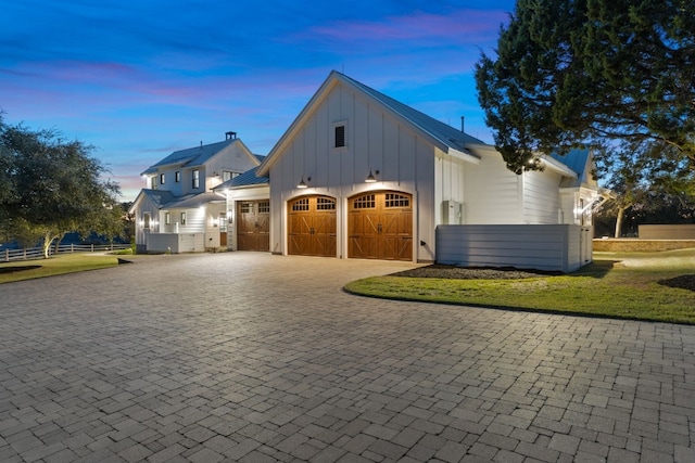 garage at dusk featuring decorative driveway and fence