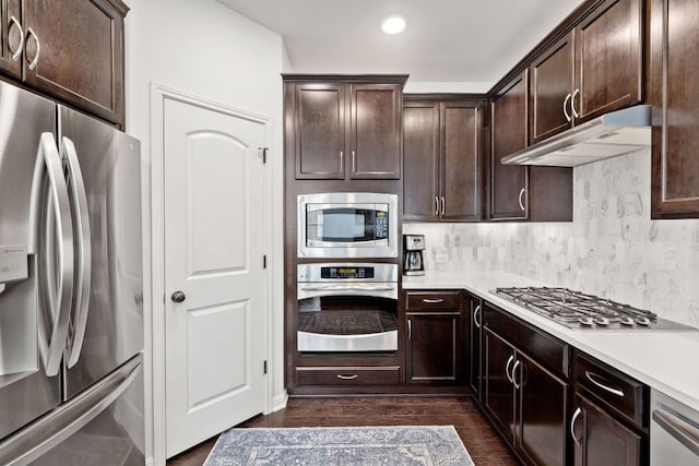 kitchen featuring under cabinet range hood, dark brown cabinetry, appliances with stainless steel finishes, light countertops, and dark wood-style flooring