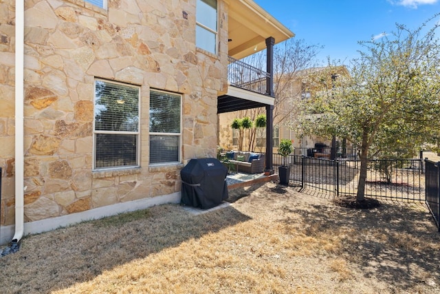 view of home's exterior featuring stone siding, a balcony, a patio, and fence