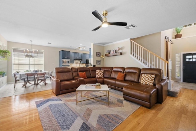 living room with light wood finished floors, visible vents, stairway, ornamental molding, and ceiling fan with notable chandelier