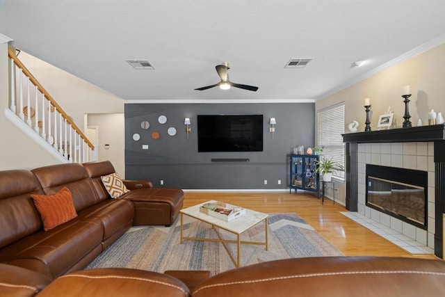 living room with visible vents, a tiled fireplace, wood finished floors, stairway, and ceiling fan