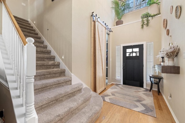 entryway with wood finished floors, stairway, a barn door, baseboards, and a towering ceiling