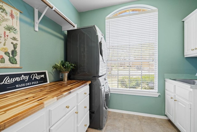 clothes washing area with baseboards, stacked washer and clothes dryer, light tile patterned flooring, cabinet space, and a sink