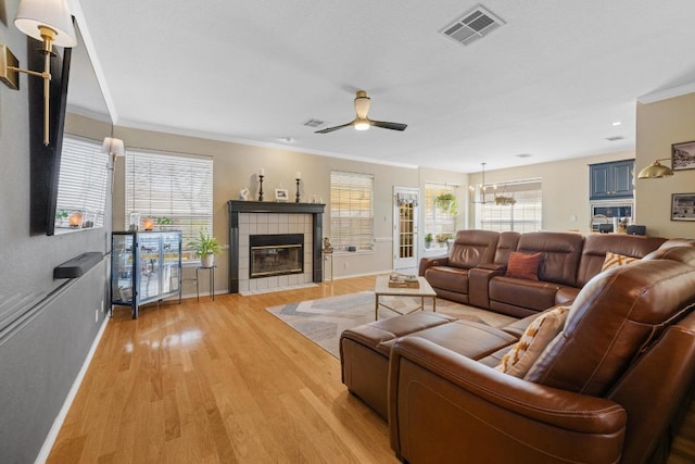 living area with visible vents, light wood-style flooring, ornamental molding, and ceiling fan with notable chandelier