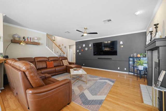 living room with visible vents, ornamental molding, a ceiling fan, light wood-style floors, and stairs