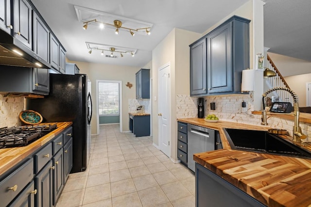 kitchen with black appliances, a sink, butcher block counters, light tile patterned floors, and extractor fan