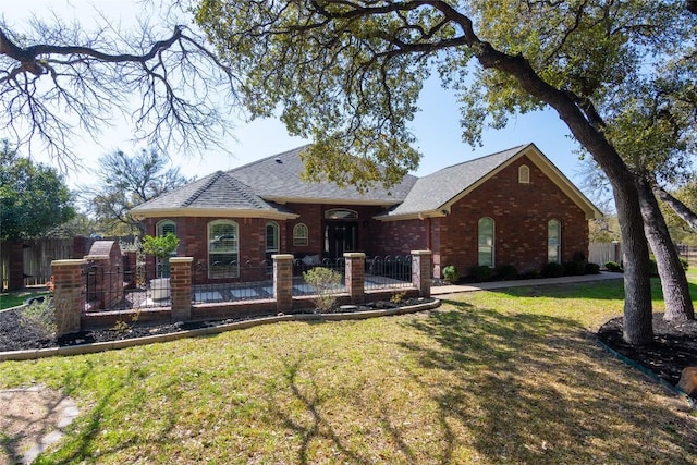 view of front facade with a fenced front yard, brick siding, a front yard, and a shingled roof