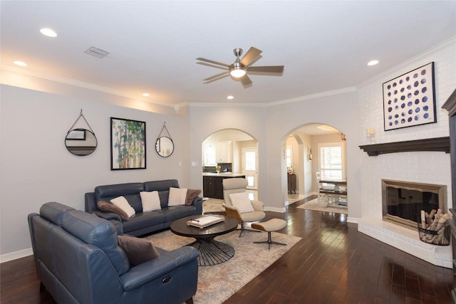 living room featuring visible vents, dark wood-style floors, arched walkways, crown molding, and ceiling fan