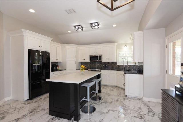 kitchen with lofted ceiling, decorative backsplash, stainless steel microwave, marble finish floor, and black refrigerator with ice dispenser