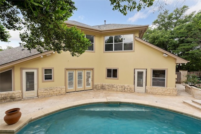 rear view of house with stucco siding, stone siding, and a patio area