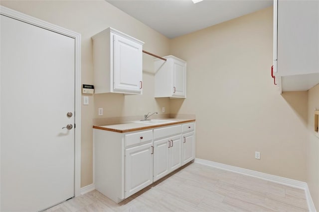 kitchen featuring a sink, baseboards, light countertops, and white cabinetry