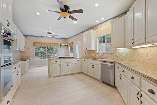 kitchen featuring a ceiling fan, a sink, backsplash, stainless steel appliances, and a peninsula