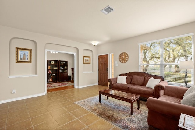 living room featuring light tile patterned floors, visible vents, arched walkways, and baseboards