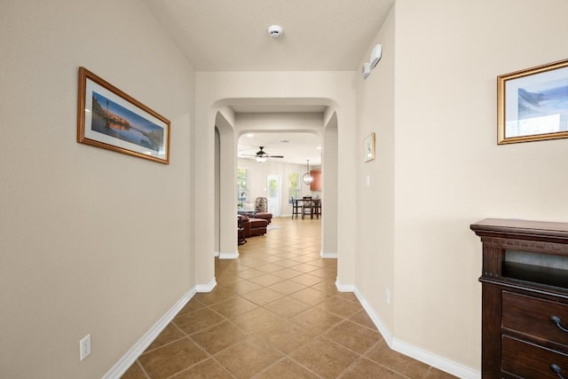 hall featuring tile patterned floors, baseboards, and arched walkways