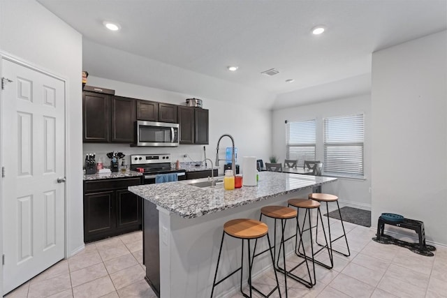 kitchen featuring light stone countertops, a kitchen bar, an island with sink, light tile patterned flooring, and stainless steel appliances