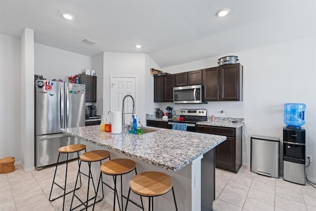 701 Taggart Trl, Jarrell, TX 76537 - kitchen with stainless steel appliances, dark brown cabinetry, a breakfast bar area, an island with sink, and light tile patterned floors