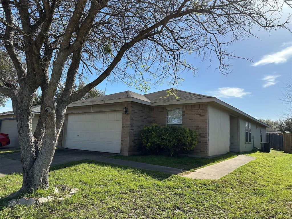 ranch-style house with a front yard, cooling unit, brick siding, and an attached garage