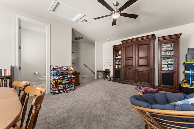 living area featuring visible vents, light colored carpet, attic access, and a ceiling fan