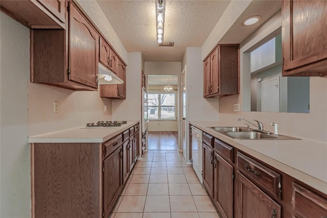 kitchen with a sink, under cabinet range hood, a textured ceiling, white appliances, and light countertops