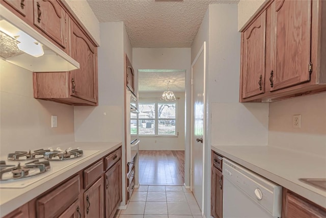 kitchen featuring under cabinet range hood, white appliances, a textured ceiling, and light countertops