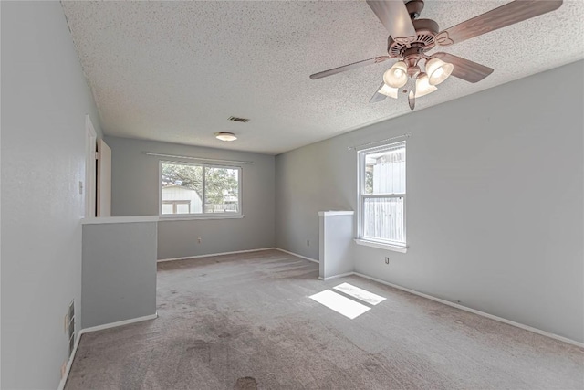 carpeted empty room with visible vents, baseboards, a textured ceiling, and a ceiling fan