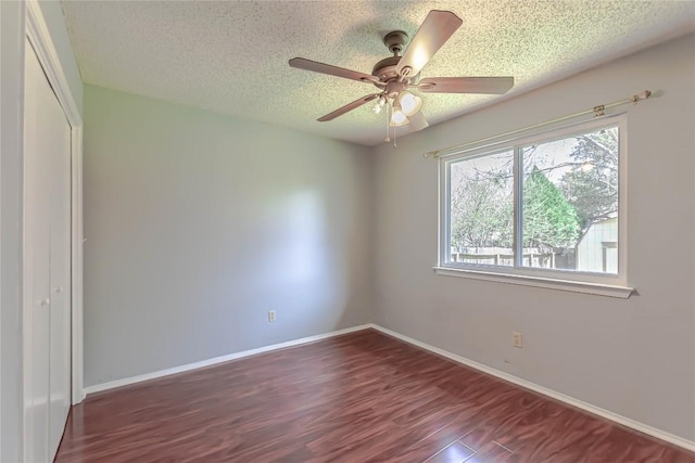 empty room with ceiling fan, wood finished floors, baseboards, and a textured ceiling