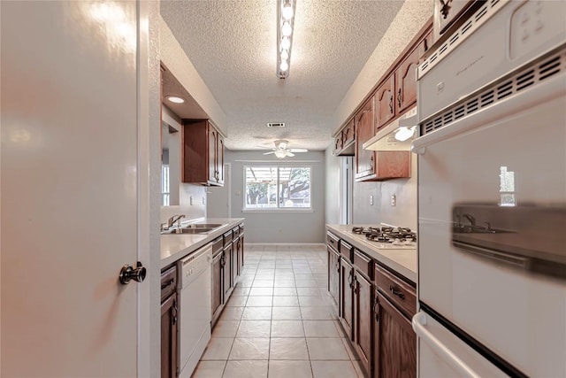 kitchen featuring under cabinet range hood, a sink, a textured ceiling, white appliances, and light tile patterned floors