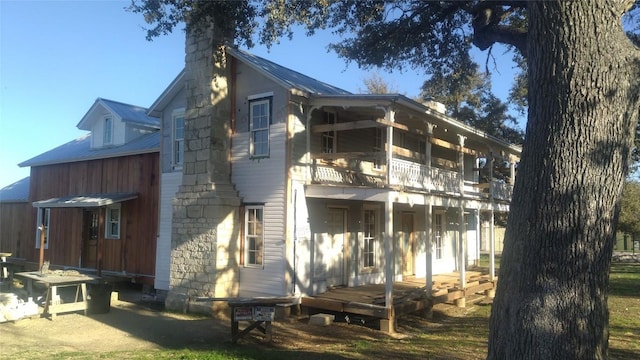 rear view of property with metal roof, a balcony, and a chimney