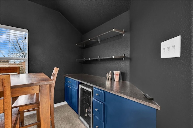 bar featuring light carpet, wine cooler, a bar, lofted ceiling, and a textured wall