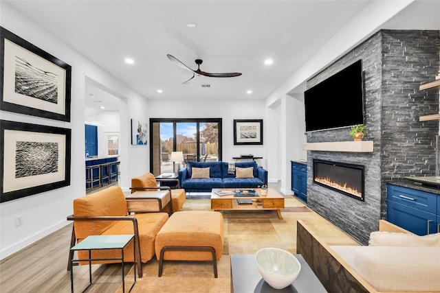 living area featuring light wood finished floors, baseboards, a stone fireplace, recessed lighting, and a ceiling fan