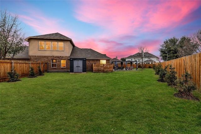 rear view of house featuring a patio, a yard, a fenced backyard, a shingled roof, and brick siding