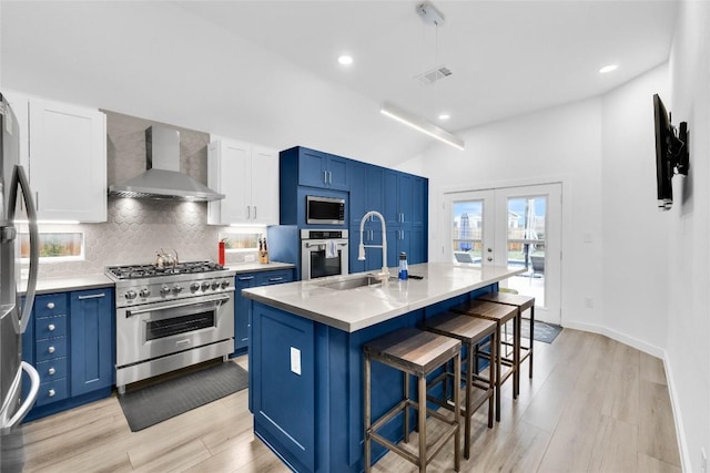 kitchen with a sink, wall chimney range hood, blue cabinets, and stainless steel appliances