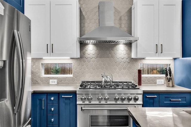 kitchen featuring blue cabinets, stainless steel appliances, white cabinets, and wall chimney range hood