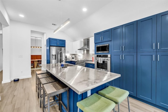 kitchen featuring visible vents, a kitchen bar, blue cabinetry, appliances with stainless steel finishes, and wall chimney exhaust hood