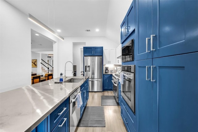 kitchen featuring blue cabinets, a sink, stainless steel countertops, stainless steel appliances, and light wood finished floors