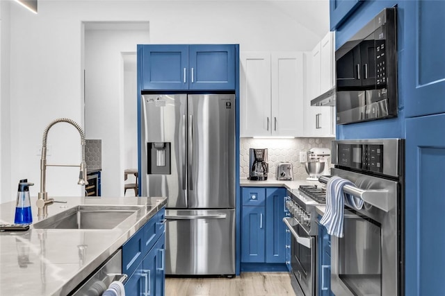 kitchen featuring a sink, under cabinet range hood, appliances with stainless steel finishes, white cabinetry, and blue cabinets