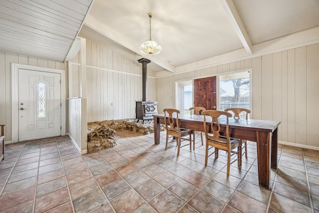 dining room featuring lofted ceiling with beams, plenty of natural light, wood walls, and a wood stove