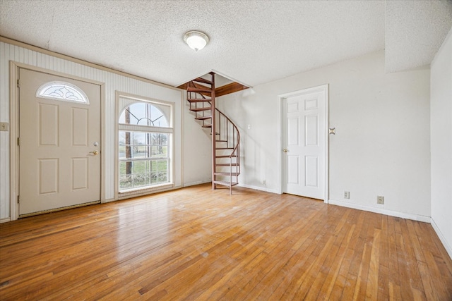 entryway featuring baseboards, light wood-style floors, stairs, and a textured ceiling